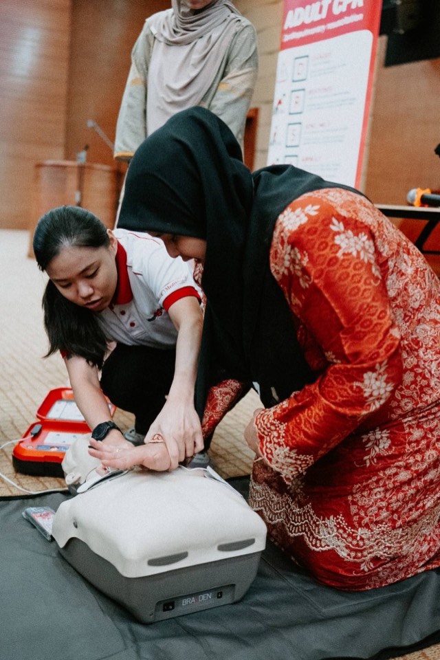 A MediShield trainer correcting hand position during CPR practice